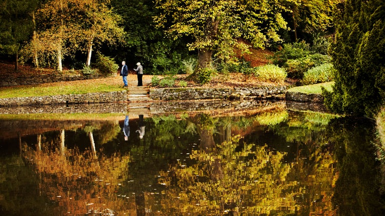 Visitors by the lake in the garden in autumn at Lyme Park, Cheshire